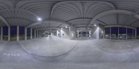 a wide angle view of the inside of an indoor parking lot at night, with multiple windows on each side