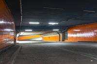 a photo of the side walk of a tunnel at night, with orange walls and lights