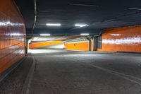 a photo of the side walk of a tunnel at night, with orange walls and lights