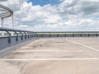 an empty parking lot under a cloudy blue sky with clouds in the background by the bridge