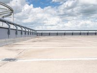 an empty parking lot under a cloudy blue sky with clouds in the background by the bridge