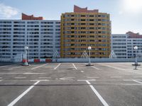 an empty parking lot filled with parking cones and buildings in the background with an orange stripe on the ground