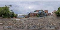 a fisheye image of a brick road with parked bikes and buildings in the background