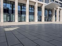 a tiled square sitting outside the top floor of a tall building with glass walls and columns