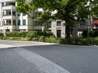 the road is cobble stone between two buildings and a sidewalk in front of a tree and bushes