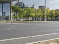 an empty city street in front of a building with trees and people sitting on benches