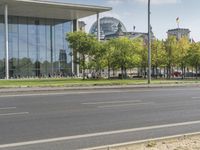 an empty city street in front of a building with trees and people sitting on benches