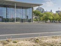 an empty city street in front of a building with trees and people sitting on benches