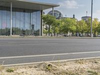 an empty city street in front of a building with trees and people sitting on benches