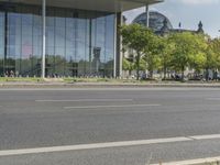 an empty city street in front of a building with trees and people sitting on benches