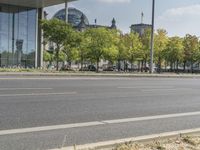 an empty city street in front of a building with trees and people sitting on benches