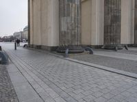 a concrete sidewalk next to two stone pillars and a sidewalk with multiple rows of black chairs