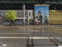 the large poster is on the side of the building by the street on a rainy day