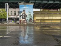 the large poster is on the side of the building by the street on a rainy day