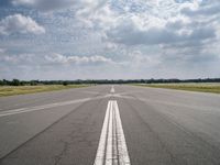 a long empty runway under a cloudy blue sky with white lines in the middle of it