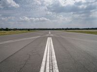 a long empty runway under a cloudy blue sky with white lines in the middle of it