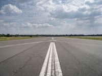 a long empty runway under a cloudy blue sky with white lines in the middle of it