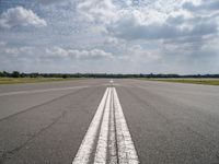 a long empty runway under a cloudy blue sky with white lines in the middle of it