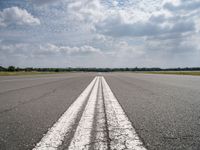 a long empty runway under a cloudy blue sky with white lines in the middle of it