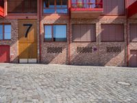 a brick patio near a building and some red buildings are near one another with a large brick wall