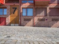 a brick patio near a building and some red buildings are near one another with a large brick wall