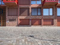 a brick patio near a building and some red buildings are near one another with a large brick wall