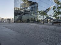 large mirrored building reflecting trees in a city park plaza with a few benches at the end