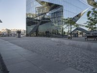 large mirrored building reflecting trees in a city park plaza with a few benches at the end