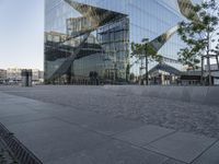 large mirrored building reflecting trees in a city park plaza with a few benches at the end