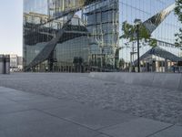large mirrored building reflecting trees in a city park plaza with a few benches at the end