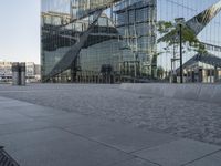 large mirrored building reflecting trees in a city park plaza with a few benches at the end