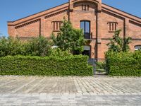 the brick building is surrounded by trees and bushes along the driveway are green plants that are planted on either side