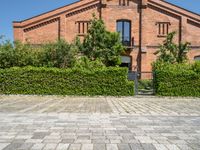 the brick building is surrounded by trees and bushes along the driveway are green plants that are planted on either side