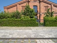 the brick building is surrounded by trees and bushes along the driveway are green plants that are planted on either side