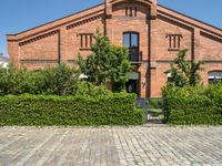 the brick building is surrounded by trees and bushes along the driveway are green plants that are planted on either side