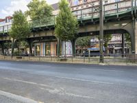 an empty street next to the river, with a bridge over it and trees on both sides