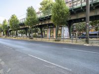 an empty street next to the river, with a bridge over it and trees on both sides