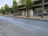 an empty street next to the river, with a bridge over it and trees on both sides