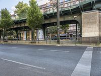 an empty street next to the river, with a bridge over it and trees on both sides