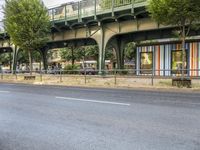 an empty street next to the river, with a bridge over it and trees on both sides