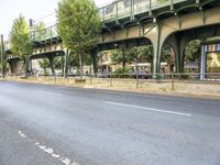 an empty street next to the river, with a bridge over it and trees on both sides