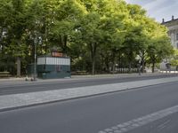 the sidewalk is lined with trees and benches on it and people walking on it next to a bus stop