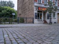 a small dog walking past a stone path outside a store front, which has a sign on its door