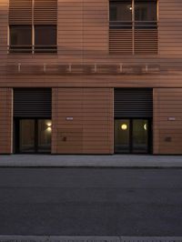 a building with four windows next to a street in front of it at dusk with light reflecting off the window