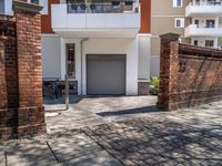 the driveway leading to a building with two brick pillars and a bike rack in front