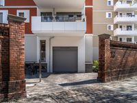 the driveway leading to a building with two brick pillars and a bike rack in front