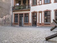 a brick sidewalk with an old metal sculpture next to a building and balcony area with several windows