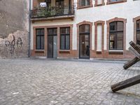 a brick sidewalk with an old metal sculpture next to a building and balcony area with several windows