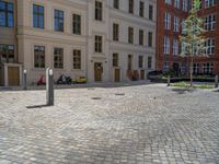 a green shrub near a gray building and a brick walkway with a bicycle rack in it