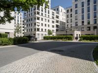 a wide paved street surrounded by tall white building facades surrounded by greenery and bushes